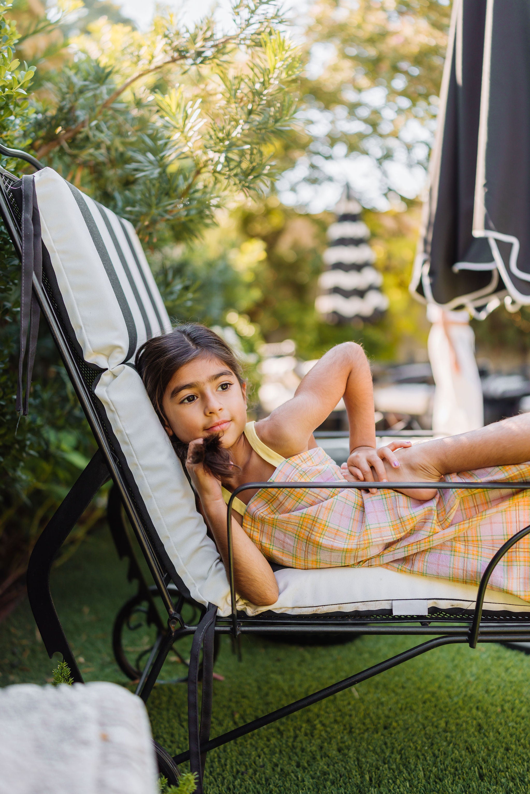 Child lying on a lounge chair outdoors with greenery in the background