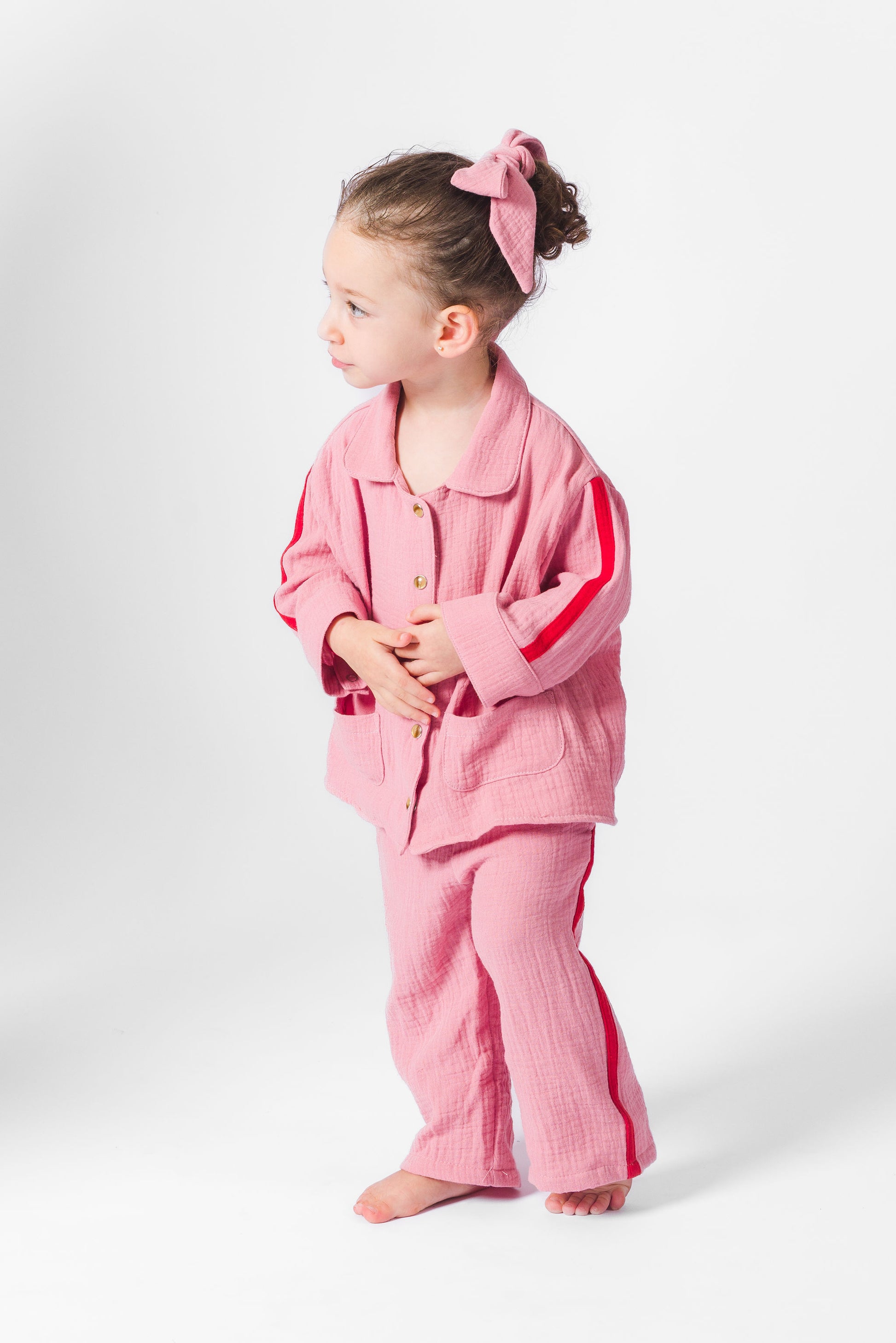 Child wearing a pink lounge wear set with a bow in hair on a white background